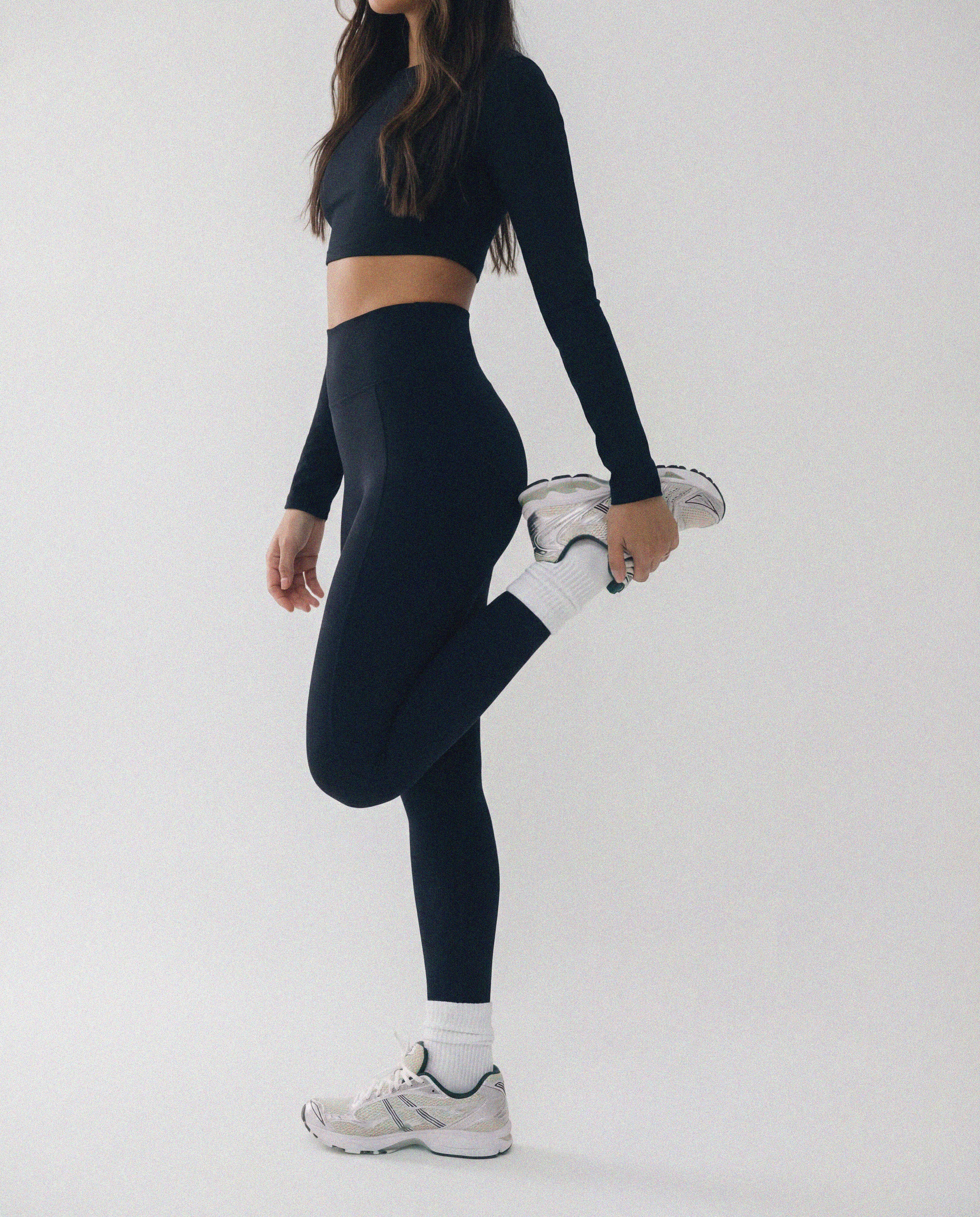 Person wearing a black athletic outfit with white sneakers on a light gray background